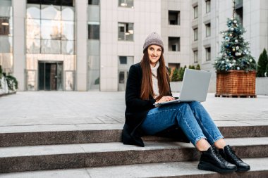 Dizüstü bilgisayarı olan bir kadın merdivenlerde oturuyor.