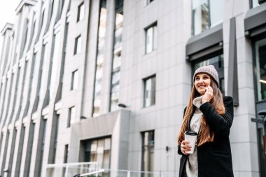 Dış giysili genç bayan telefonda konuşuyor.