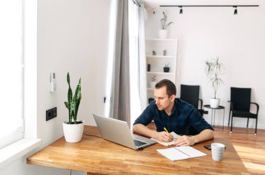 Genç adam evde dizüstü bilgisayar kullanarak çalışıyor..