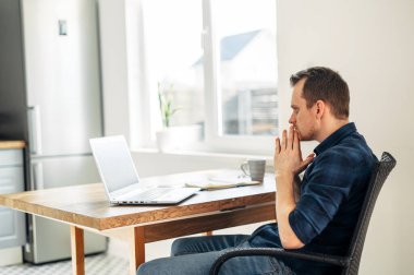 Genç adam evde dizüstü bilgisayar kullanarak çalışıyor..