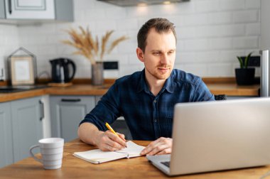 Genç adam evde dizüstü bilgisayar kullanarak çalışıyor..