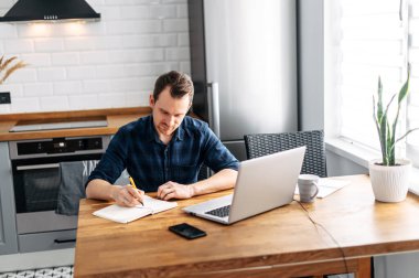 Genç adam evde dizüstü bilgisayar kullanarak çalışıyor..