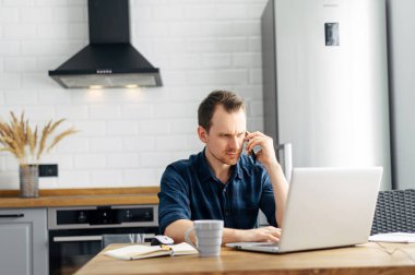 Genç adam evde dizüstü bilgisayar kullanarak çalışıyor..