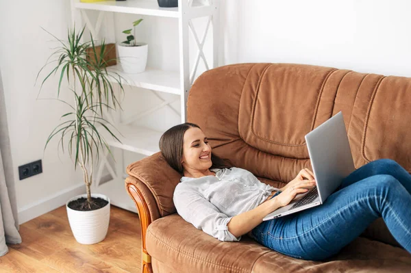 Een vrouw ligt thuis op de bank met een laptop — Stockfoto