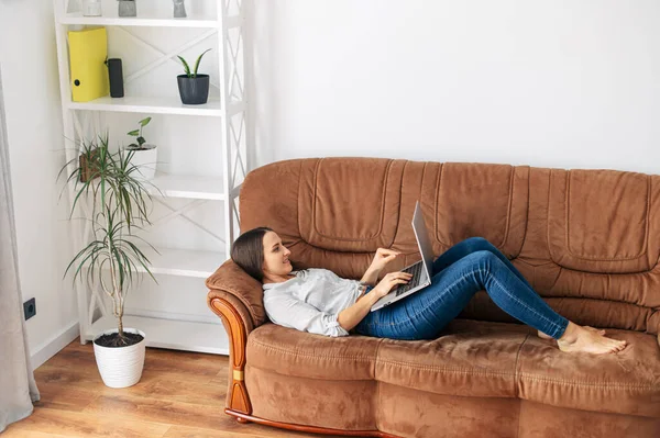 Een vrouw ligt thuis op de bank met een laptop — Stockfoto