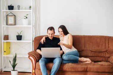 Kanepede dizüstü bilgisayarı olan genç evli bir çift.