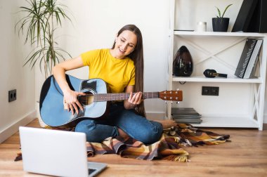 Bir kadın gitar çalarken video dersi izliyor.