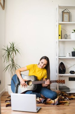 Bir kadın gitar çalarken video dersi izliyor.