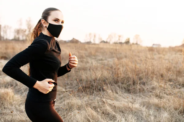 Kvinner i svart sportstøy og masker løper utendørs. – stockfoto