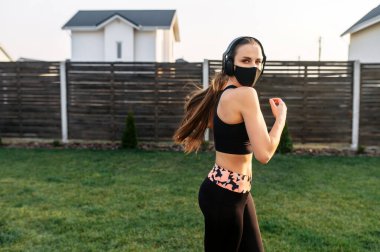 Maskeli kadın arka bahçede kardiyo çalışması yapıyor.