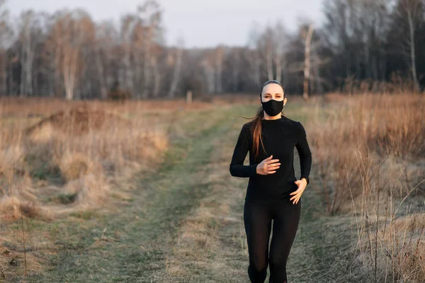 Kvinner i svart sportstøy og masker løper utendørs. – stockfoto