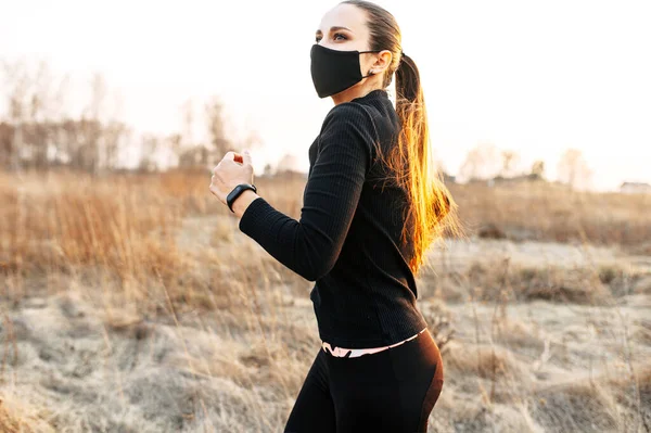 Жінка в чорному спортивному одязі і масці працює на відкритому повітрі — стокове фото