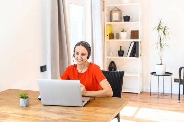 Kadın evde kulaklık ve dizüstü bilgisayar kullanarak çalışıyor.