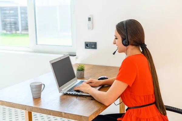 Woman works from home using headset and laptop