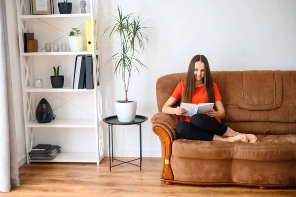 Frau sitzt auf dem Sofa und liest ein Buch — Stockfoto