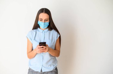 Akıllı telefonlu, tıbbi maskeli genç bir kadın.