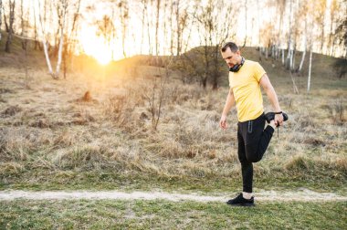 Kulaklıklı çekici adam dışarıda egzersiz yapıyor.