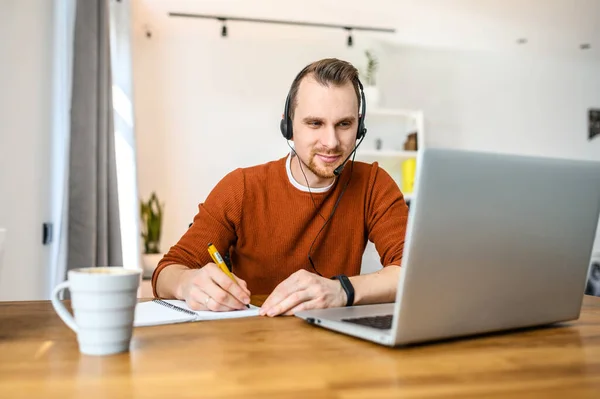 Guy olha para laptop e notas no notebook — Fotografia de Stock