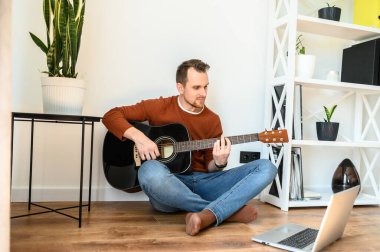 Bir adam gitar çalarken video dersi izliyor.