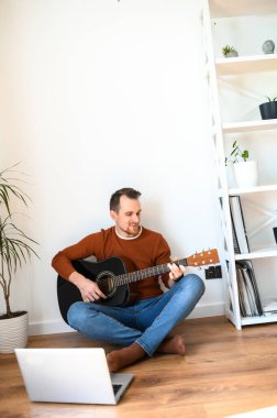 Bir adam gitar çalarken video dersi izliyor.