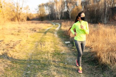 Woman in medical mask is jogging outdoors clipart