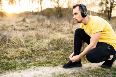 Kulaklıklı atletik adam ayakkabı bağcığı takıyor.