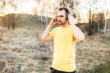 Kulaklıklı atletik adam açık havada müzik dinliyor.