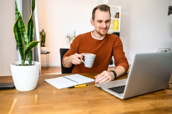 Positieve kerel zit aan de tafel en maakt gebruik van een laptop — Stockfoto