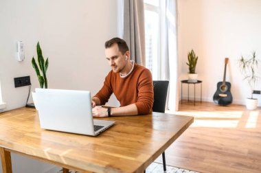 Adam dizüstü bilgisayara ve not defterine bakıyor.