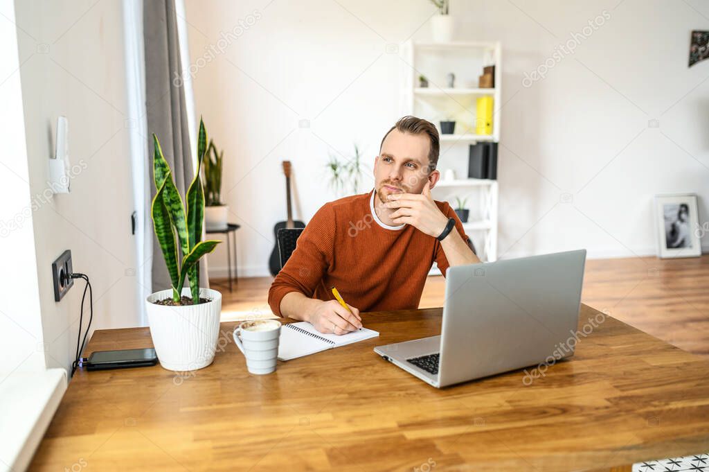 Positive guy sits at the table and uses a laptop