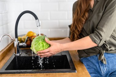 Bir kadın akan suyun altında lahana yıkıyor.