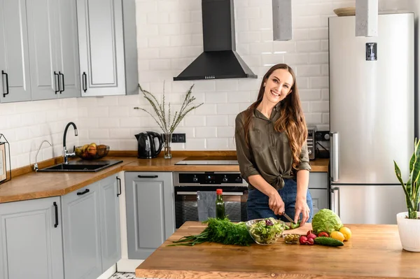 Uma jovem mulher feliz preparando uma salada em casa — Fotografia de Stock