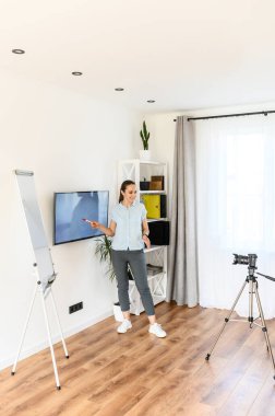 Okul dersleri çevrimiçi. Bir bayan öğretmen video dersleri kaydediyor. Açıklama için grafik ve monitör kullanıyor.