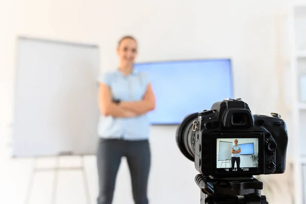 Une femme enregistre des cours vidéo à la maison pour étudier à distance, elle utilise un tableau à feuilles mobiles et un moniteur. Caméra sur trépied au premier plan. La femme est hors de propos — Photo