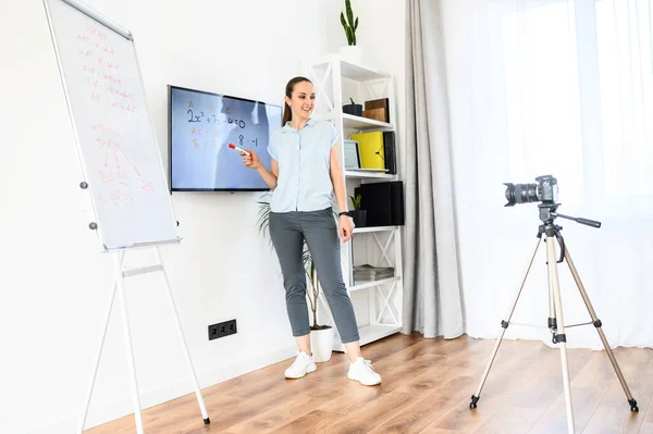 Una mujer está grabando video tutorial en casa, utiliza rotafolio y monitor. Cámara en trípode delante de la mujer. Concepto de estudio en línea — Foto de Stock