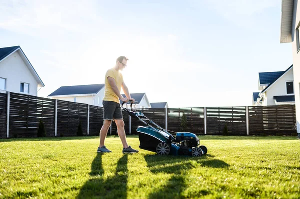 A young guy mows a lawn with a lawn mower — Stock Photo, Image