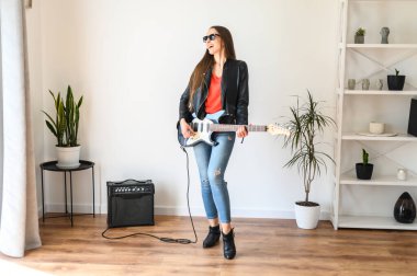 Deri ceketli kadın elektro gitar çalıyor.