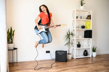 Genç kadın elektro gitarla zıplıyor.