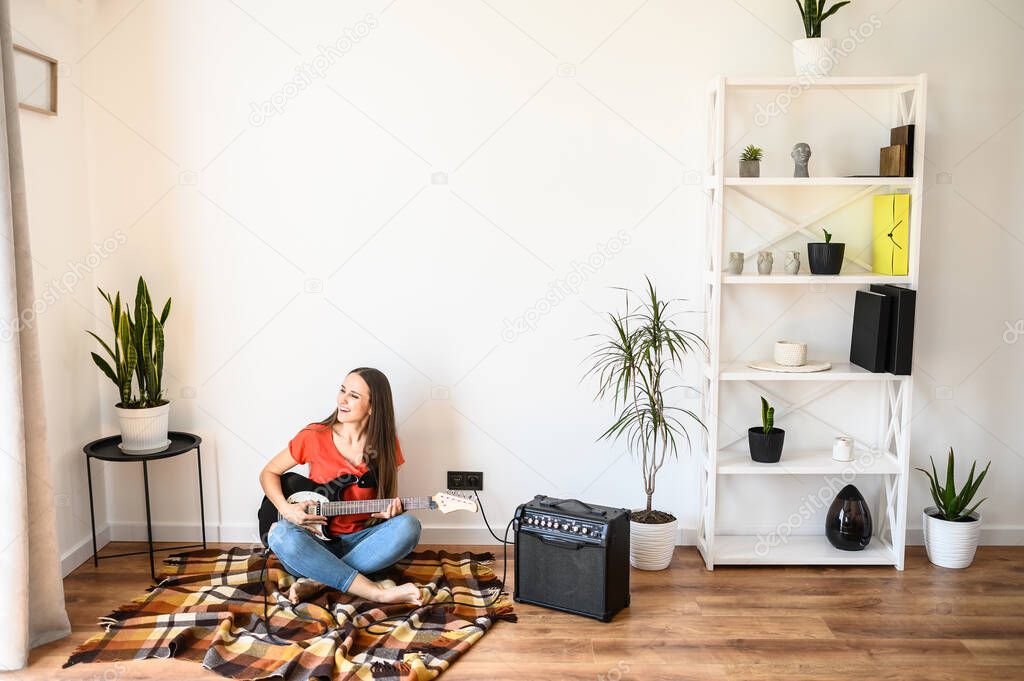Young woman plays electric guitar at home