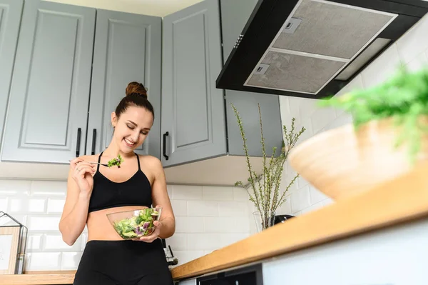Ung kvinna äter salat i köket — Stockfoto