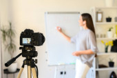 Vzdělávací video blogování, online školení. Mladá žena nahrává videa na kameru. Stojí u flipchartové tabule, ukazuje na ni a něco vysvětluje. Zaměření na obrazovku