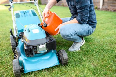 Günlük kıyafetli genç adam çim biçme makinesini dolduruyor.