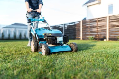 Ekose gömlekli ve kot pantolonlu genç adam çimleri biçiyor.