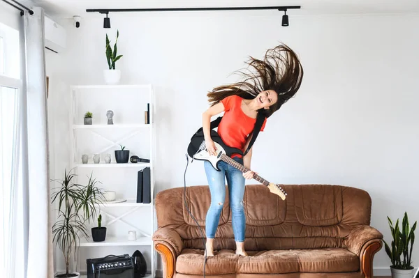 woman with an electric guitar dances on a sofa