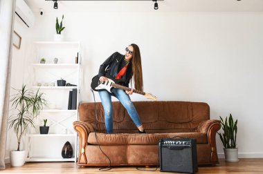 Elektro gitarlı bir kadın kanepede dans ediyor.