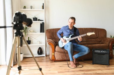 Bir adam elektro gitar çalmayı videoya kaydediyor.