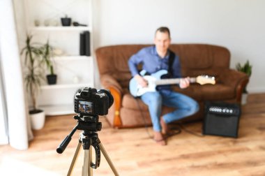 Bir adam elektro gitar çalmayı videoya kaydediyor.