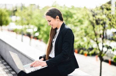 Dışarıda çalışmak için dizüstü bilgisayar kullanan genç bir kadın.