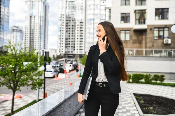 En ung kvinna med laptop pratar i telefon. — Stockfoto