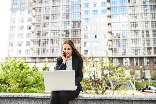 Bilgisayarlı genç bir kadın telefonda konuşuyor.